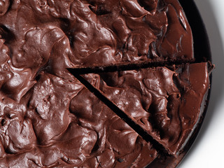 Overhead shot of a cut chocolate cake on a wooden plate and white background