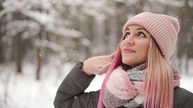 Slow motion, winter woman in the woods watching the snow fall and smiling looking at the sky and directly into the camera.