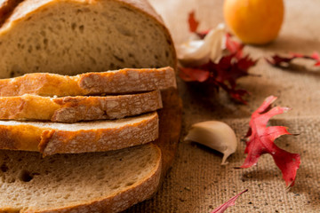 Fototapeta na wymiar Pokorojony świeży chleb w kompozycji z jesiennymi liśćmi i czosnkiem.