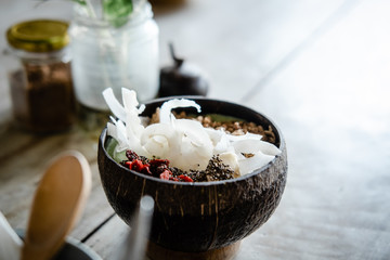 Green smoothie bowl with goji, coconut chips and granola topping on light wooden table. Food...