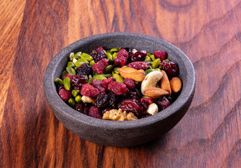 Various dried fruits and nuts in a ceramic bowl (walnut, cashew, almonds, pine nuts, hazelnuts) on a gray stone or slate background. The concept of a healthy dessert.