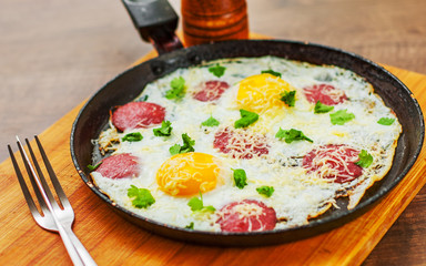 fried egg with ham sausage and cheese in a frying pan on wooden table background