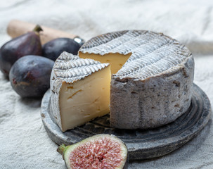 Round mature French Tomme cheese with cutted piece close up