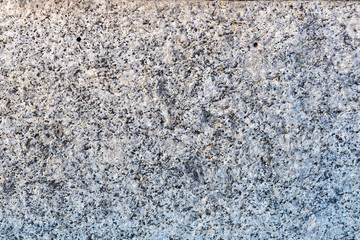 A close-up of a surface of treated grey granite rock plate. A fragment of a stone wall decoration. Texture of bright grey granite facing material.