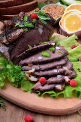 Baked ham of elk meat cut into slices topped with greenery and cranberries on the salad leaves