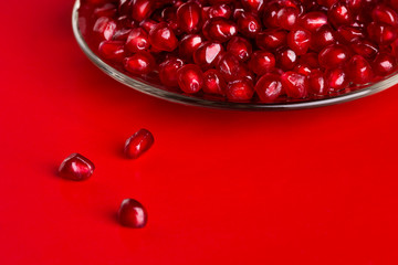 Pomegranate seeds in a plate on a red background.