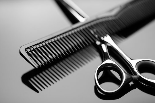Barber scissors and a hairbrush closeup on the mirror surface of the table. Barber scissors close up.