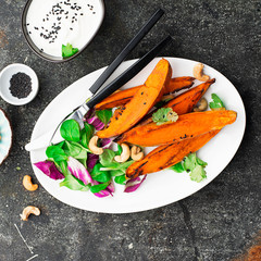 Seasonal fresh salad with baked sweet potatoes, lettuce, cashews, radicchio on a white oval dish....