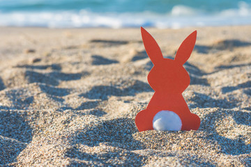 Creative easter concept photo of red paper bunny on the sand on the beach at sunset. Concept....