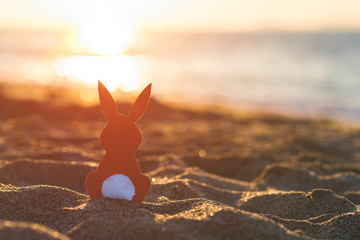 Creative easter concept photo of red paper bunny on the sand on the beach at sunset. Concept....