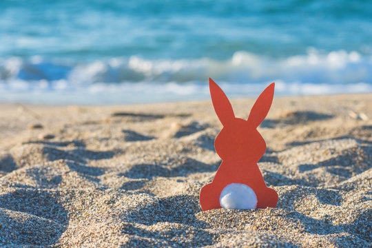 Creative easter concept photo of red paper bunny on the sand on the beach at sunset. Concept of Easter celebrations in tropical countries.