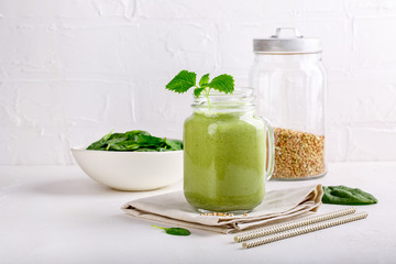 Green smoothie drink in glass jar on white. Mixed cocktail with spinach and green buckwheat.