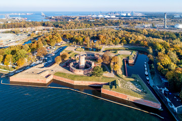 Medieval Wisloujscie Fortress with old lighthouse tower in port of Gdansk, Poland. A unique monument of the fortification works. Aerial view at sunset. Exterior Northern  Gdansk port in the background
