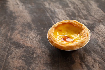 Egg tarts in aluminum foil cup on wood table,  traditional Portuguese dessert served in coffee shop