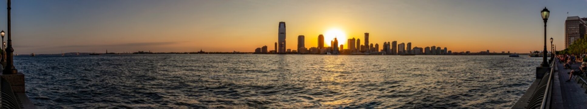 ew York / USA - 06-01-2016; A panorama photo during sunset looking from Hudson River Greenway on the Hudson River and the sun setting between the sky-line of Jersey City, New York, USA