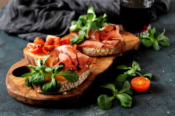 Bruschetta set with prosciutto, tomato light cheese, fresh salad and balsamic creme served with red wine. Top view with copy space.