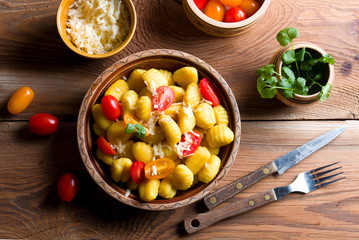 Delicious Italian gnocchi with tomatoes and cheese on wood.