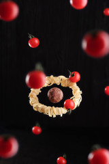 Flying food. Levitation of pasta fettuccine with meatball and tomatoes on black wooden background. Concept of meatball as a planet and spaghetti as a ring system around a planet. © bigbaraboom
