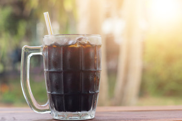 Soft drink iced Cola in A glass side view on wooden desk with green natural out door background during day time in summer