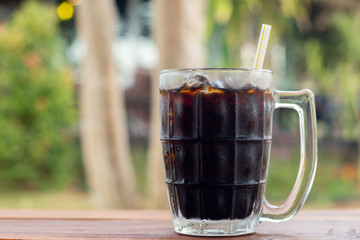 Soft drink iced Cola in A glass side view on wooden desk with green natural out door background...