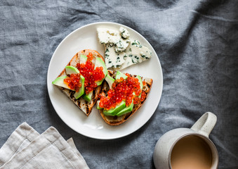 Delicious breakfast or snack - red caviar, avocado sandwiches, blue cheese and coffee on grey background, top view