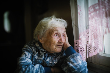 Elderly woman in the house sitting at the table looking out the window.