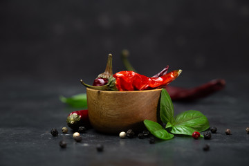 chili peppers with basil and peppercorns in bowls on a rustic surface,