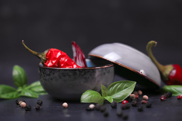 chili peppers with basil and peppercorns in bowls on a rustic surface,