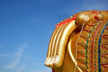 Close up of large golden buddha right hand statue and holy thread on right knee with cloud and blue...