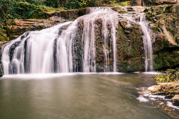 Fototapeta na wymiar A running waterfall of river through the rocks of the mountain in autumn.