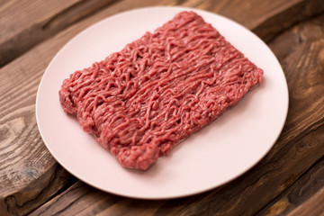 Fresh minced meat on a plate on a wooden background for cooking.