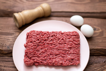 Fresh minced meat on a plate on a wooden background for cooking.