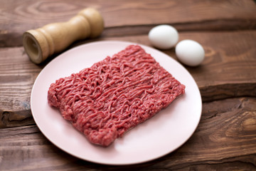 Fresh minced meat on a plate on a wooden background for cooking.
