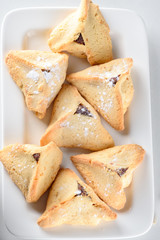 Hamantaschen cookies on white dish on wood desk colorful confetti background. Purim holiday celebration.Top view.