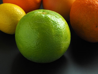 Green grapefruit, lemon and oranges on a dark background