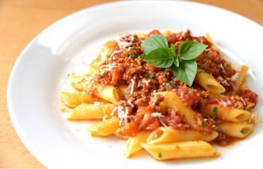 Penne  bolognese with basil leaf on white plate.
