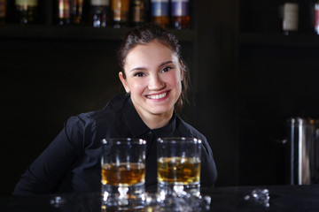 The bartender girl smiles and pours whiskey into glasses and adds ice. Photo on the bar in the restaurant. The girl is cheerful and good-natured offers to try a drink.