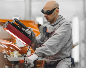 The worker of shop of coloring carries out drying of a varnish by means of a special lamp
