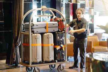 Close-up many suitcases on hotel luggage cart moving by bell boy. Baggage porter or bell boy...