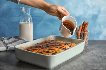 Woman pouring chocolate syrup onto freshly baked cinnamon rolls on table, closeup