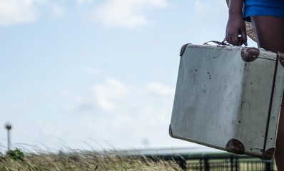 Refugee girl standing with her old suitcase on the countryside