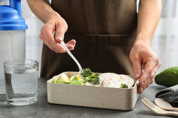Woman putting natural protein food into container on gray table, closeup