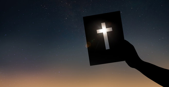 Hand h&auml;lt die Bibel vor dunklem Himmel