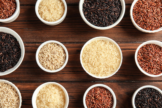 Bowls with different types of rice on wooden background, top view