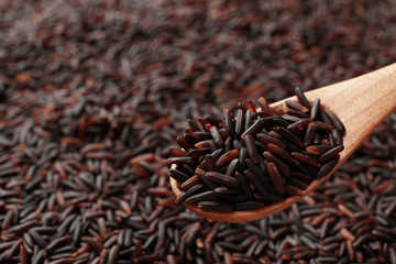 Wooden spoon with raw brown rice over cereal, closeup