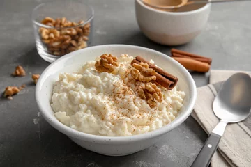 Poster Creamy rice pudding with cinnamon and walnuts in bowl served on grey table © New Africa