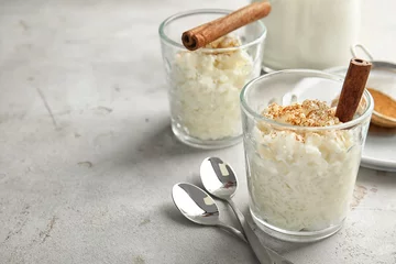Poster Creamy rice pudding with cinnamon in glasses served on grey table. Space for text © New Africa