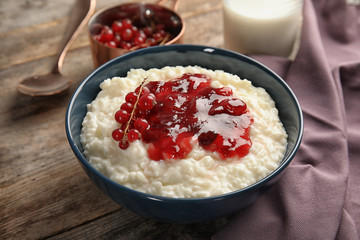 Creamy rice pudding with red currant and jam in bowl served on wooden table