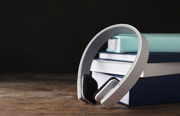Modern headphones with hardcover books on wooden table. Space for text