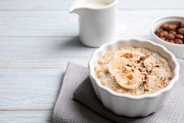 Quinoa porridge with banana and nuts in bowl served for breakfast on white wooden table. Space for text